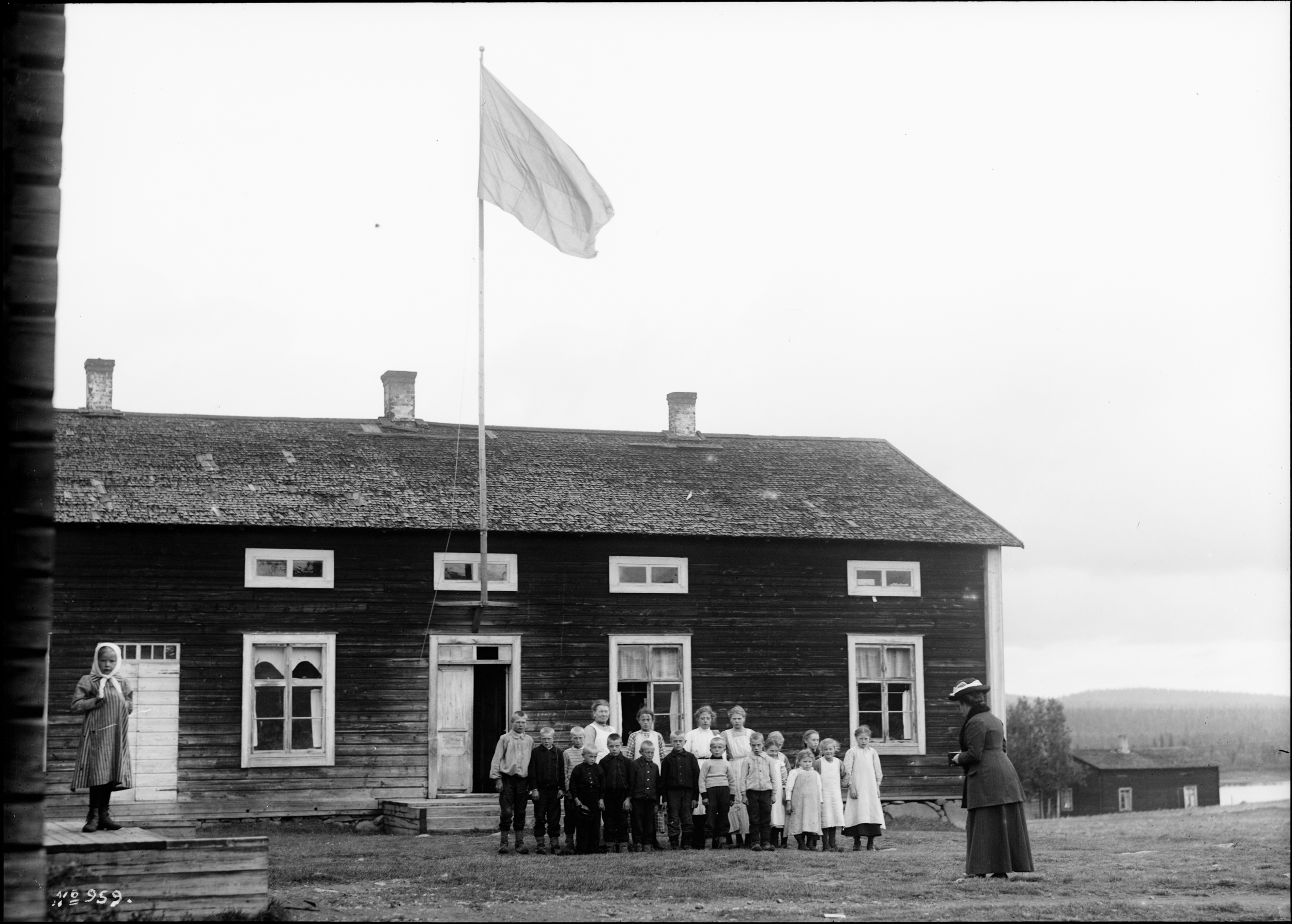 Svartvitt foto av en grupp barn som står framför ett större trähus.