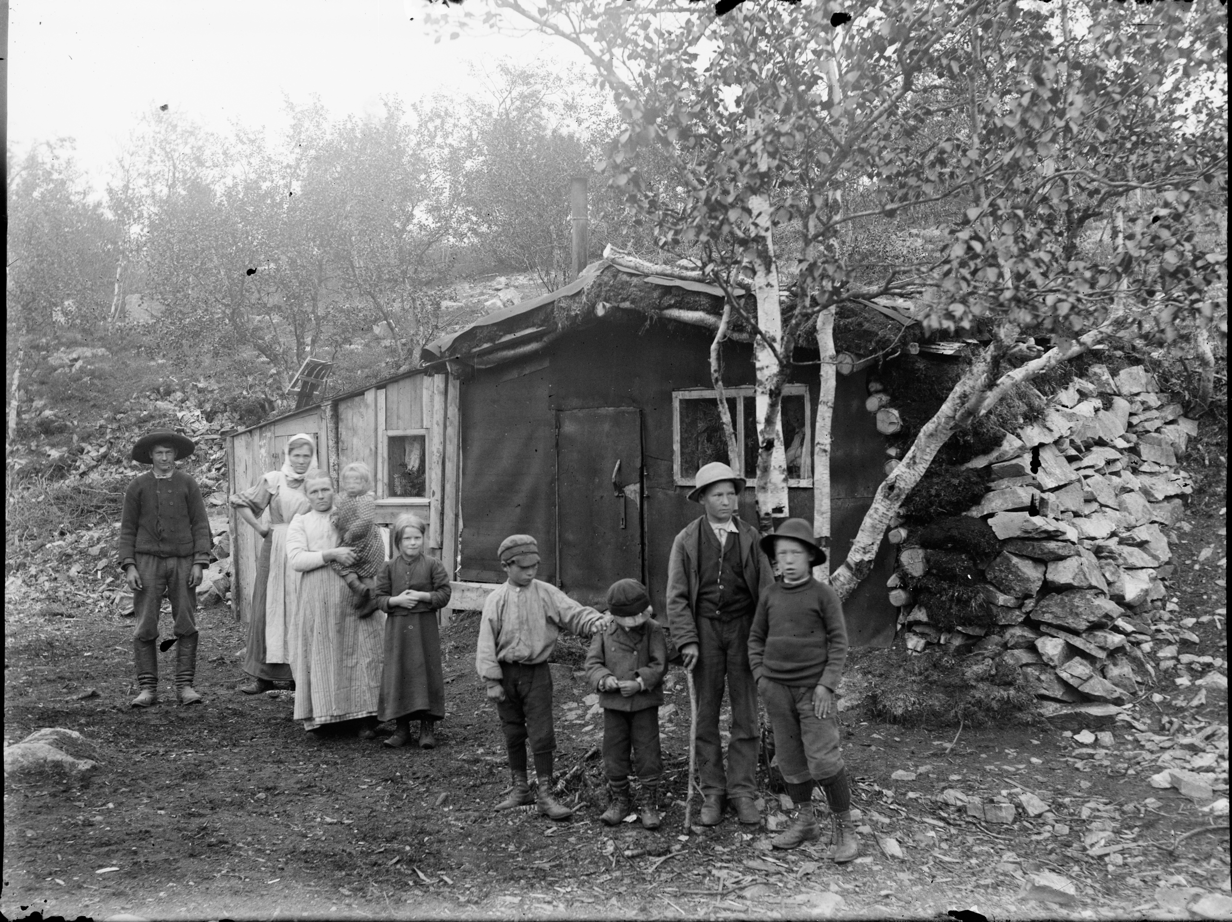 Svartvitt foto av en familj som ser ut att vara ganska fattig utanför en mycket enkel bostad.