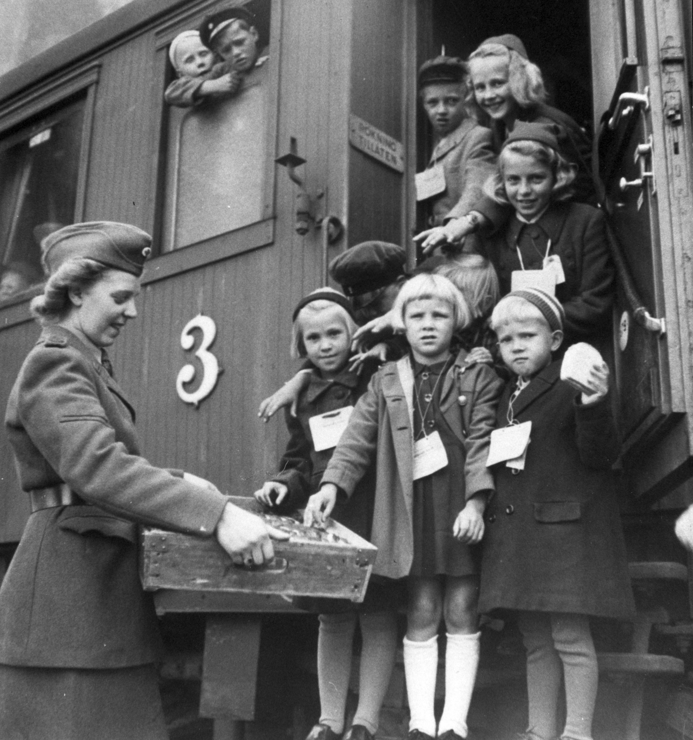 Finska krigsbarn stiger av ett tåg i Sverige 1945, där de möts av en kvinna i uniform. Många av barnen har lappar som hänger runt halsen.