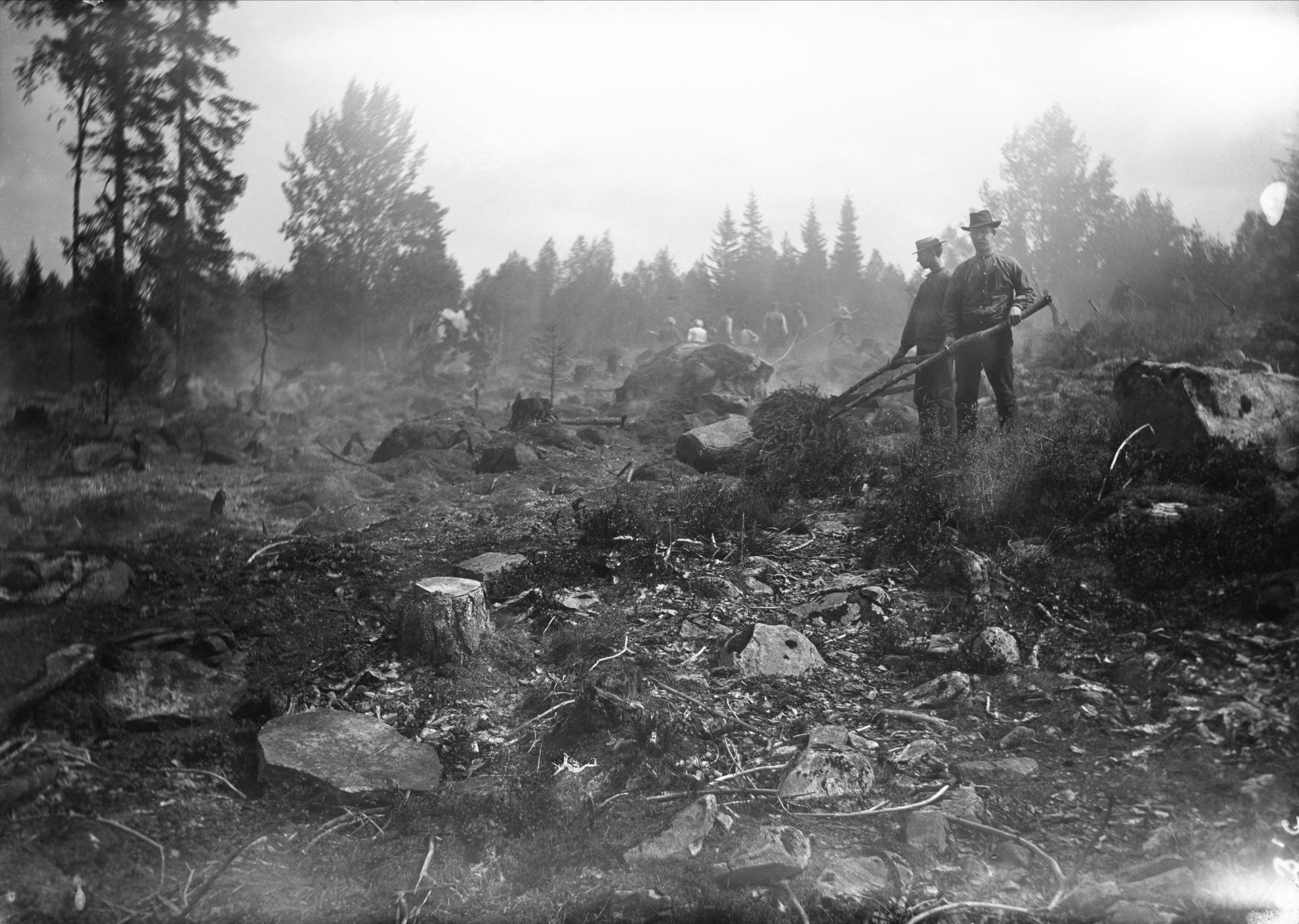 Svartvitt foto föreställande två män i färd med att bränna marken i en skog.